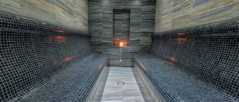 Un spa con una chimenea central, paredes con azulejos y bancos a los lados.