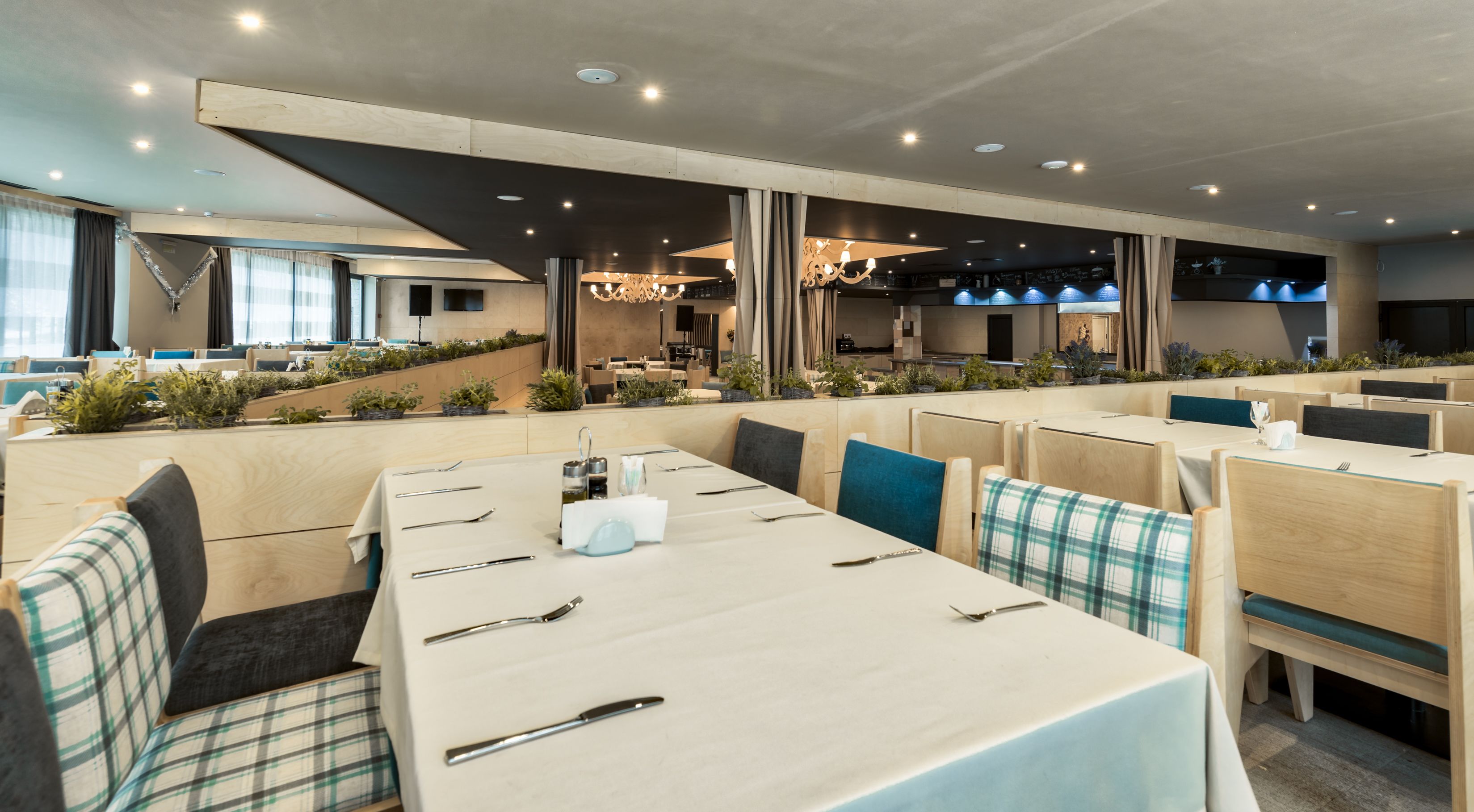 Un restaurant moderne avec de longues tables communes et des banquettes, un espace cuisine à l’arrière-plan et une vue sur le paysage urbain.