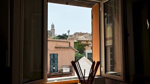 A room with a view of a cityscape through an open window, a table with a glass of water, and a vase with chopsticks. - Romantica Mansarda Pisano (Genoa)