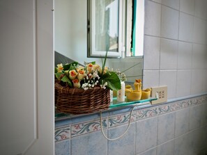 A wicker basket with flowers and a small vase on a bathroom counter. - Romantica Mansarda Pisano (Genoa)