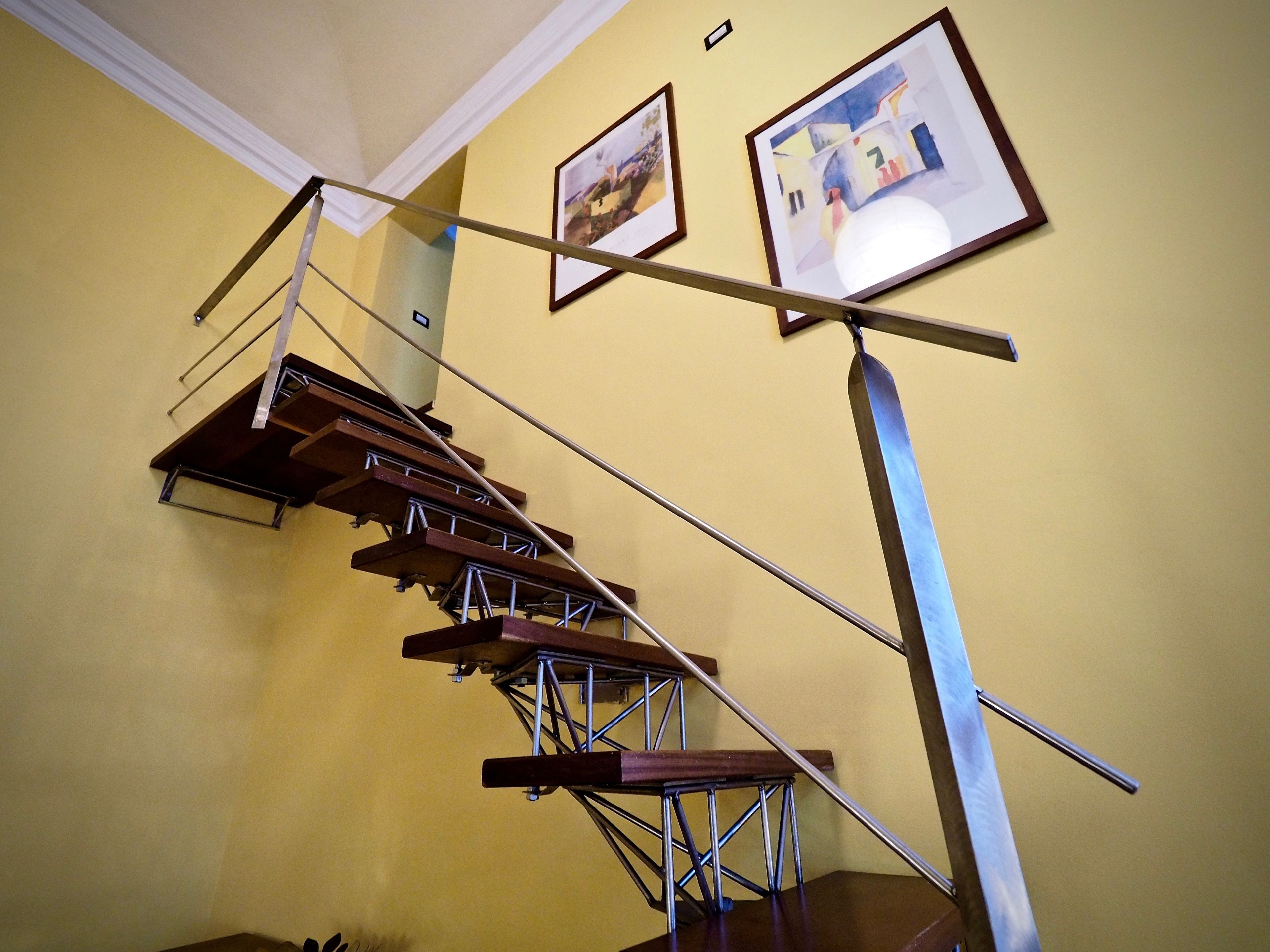 Una escalera con barandilla de metal y peldaños de madera, que conduce a un rellano con dos cuadros en la pared.
