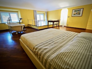 A hotel room with a large bed, a small table, a chair, a bathtub, and a window with curtains.