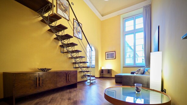 A living room with a wooden floor, a round glass coffee table, a sofa, a staircase with metal railings, and a window with curtains. - Dimora Lusso delle Vigne (Genoa)