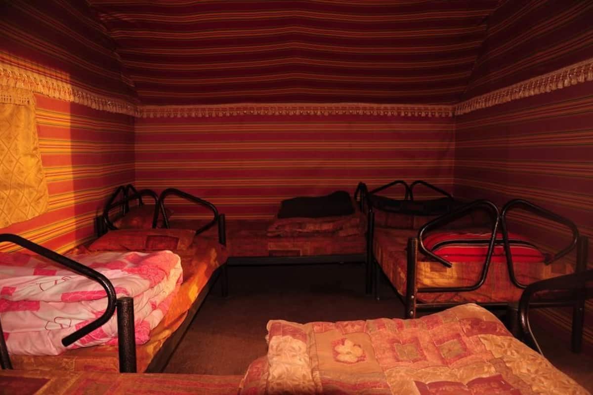Um quarto com três beliches de metal, cada um com colchão e almofadas.