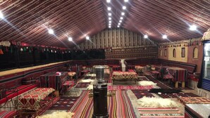 Un salón amplio con filas de asientos, un calentador central y alfombras estampadas en el suelo.