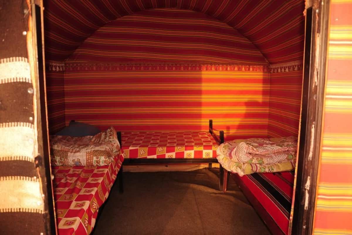 Quarto pequeno e acolhedor com duas camas, cada uma com roupa de cama estampada. O quarto possui um design de parede listrada e teto inclinado.