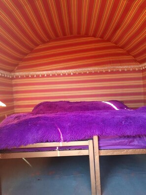 Een kamer met een bed bekleed met paars beddengoed, gestreepte wanden en een houten hoofdbord.