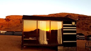 Una pequeña estructura cerrada con ventana y cortinas, ubicada en un paisaje desértico con un atardecer.