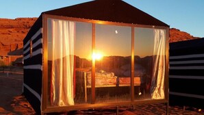 Una tienda de paredes de vidrio con una cama en su interior, frente a un paisaje desértico.