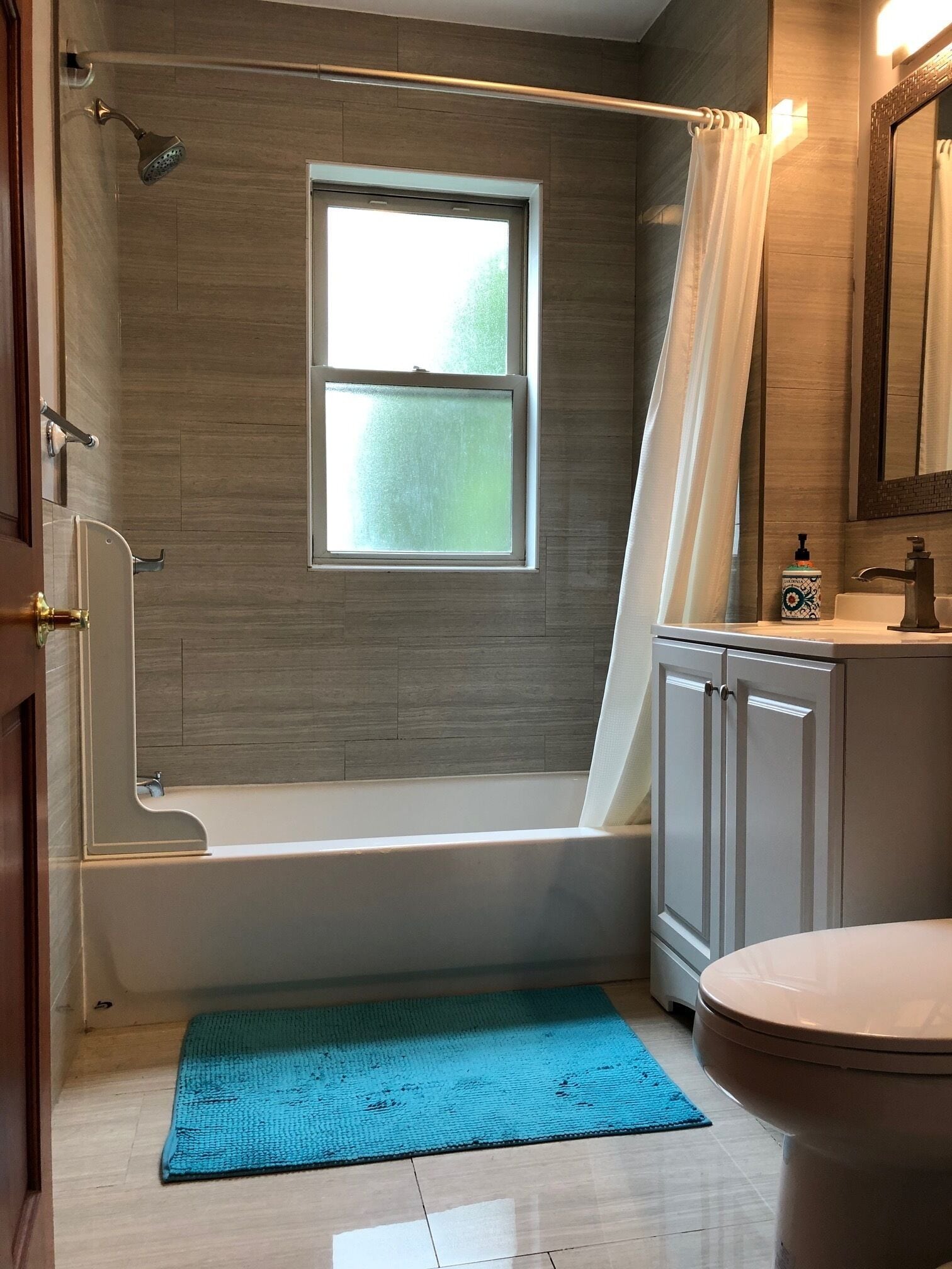 A bathroom with a bathtub, a window, a shower, a toilet, and a sink.