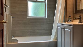 A bathroom with a bathtub, a window, a shower, a toilet, and a sink.