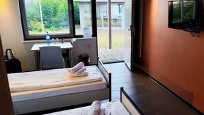 Une chambre d’hôtel avec deux lits, un bureau, une chaise, une télévision et une fenêtre donnant sur un espace verdoyant.