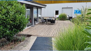 Un bâtiment moderne doté d’une terrasse en bois, de sièges extérieurs et d’un extincteur placé près de l’entrée.