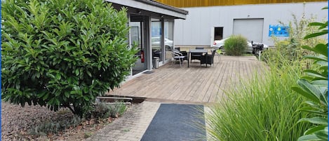 A modern building with a wooden deck, outdoor seating, and a fire extinguisher near the entrance.