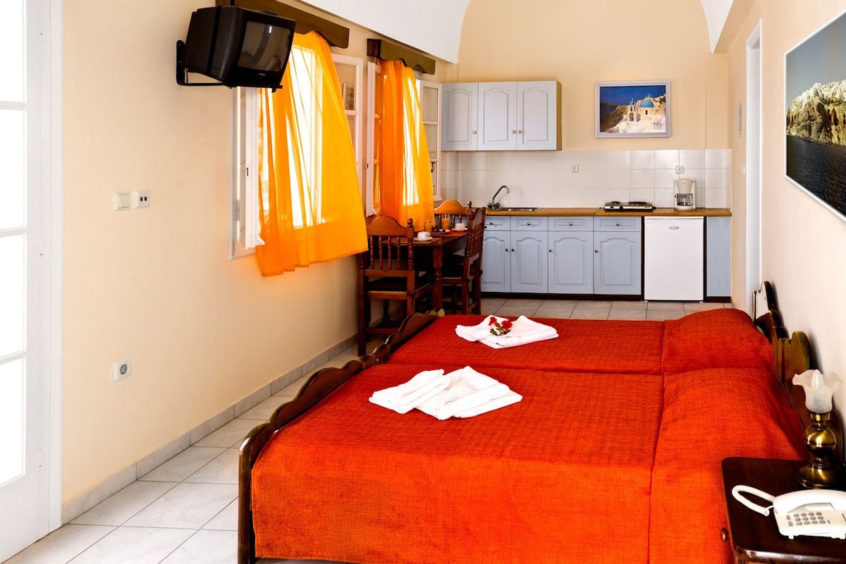 A hotel room with a bed, a desk, a chair, a television, a kitchen area, and a bathroom.