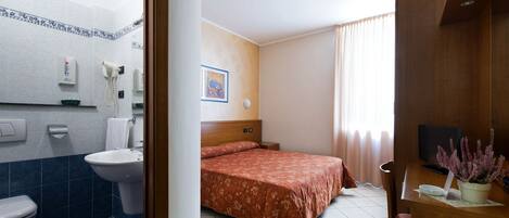 Habitación de hotel con cama, televisor, escritorio y baño con inodoro y lavamanos.