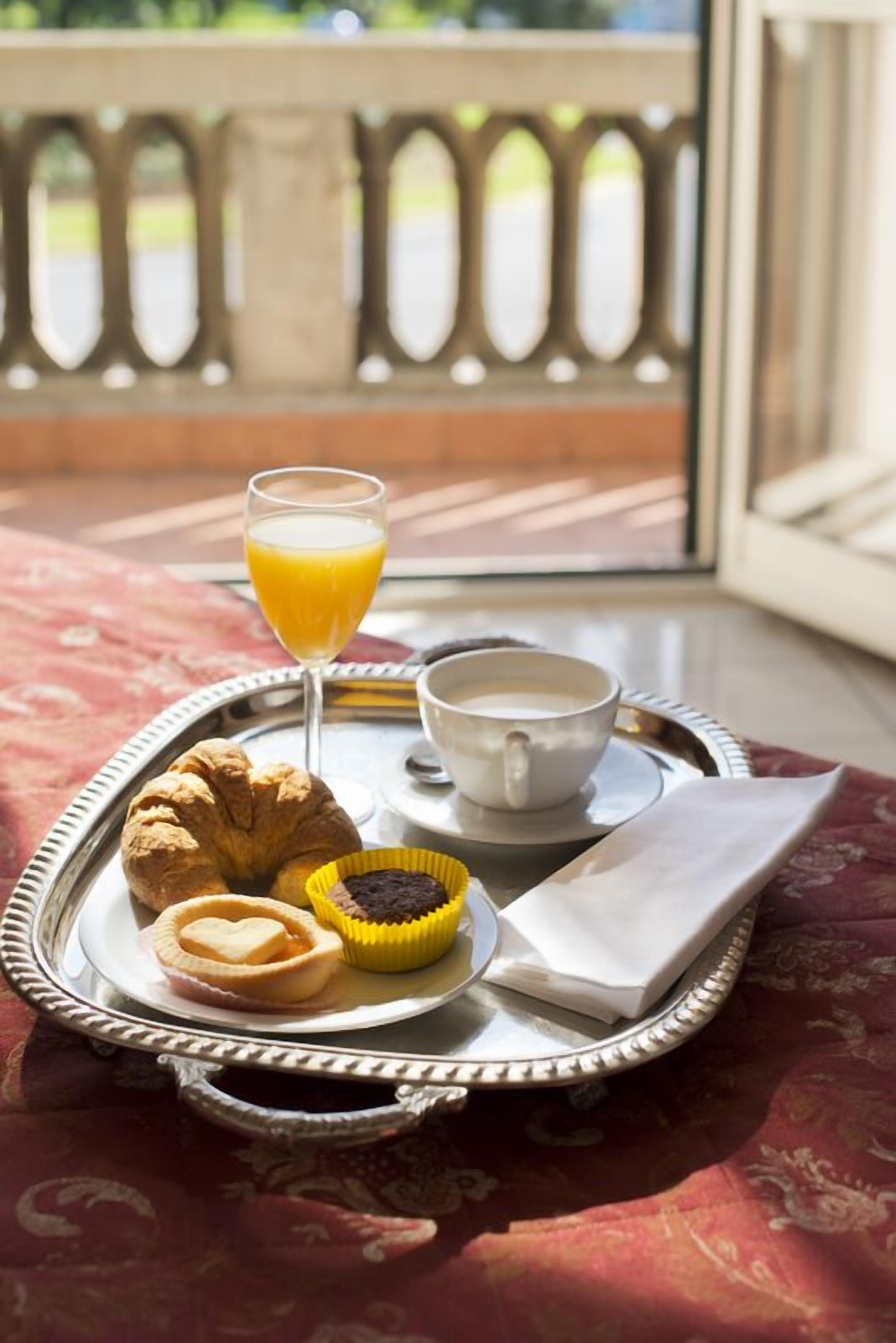 A tray with croissants, a muffin, a glass of orange juice, and a cup of coffee on a table with a red patterned tablecloth.