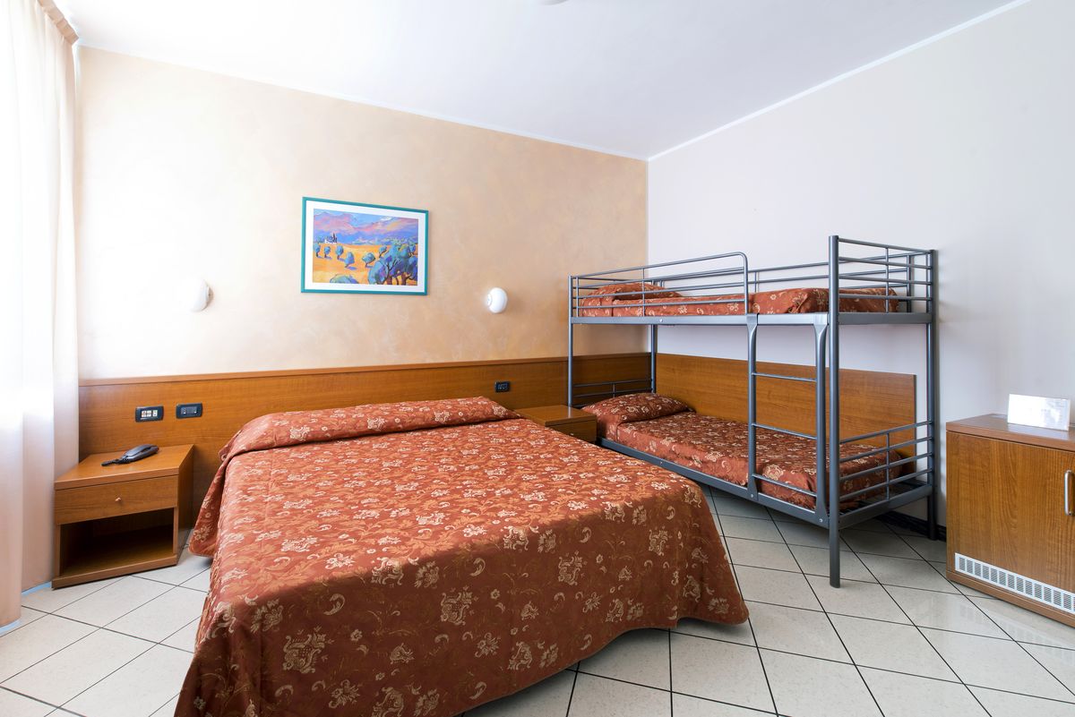 A hotel room with a bunk bed, a single bed, a wooden nightstand, a small cabinet, and a painting on the wall.