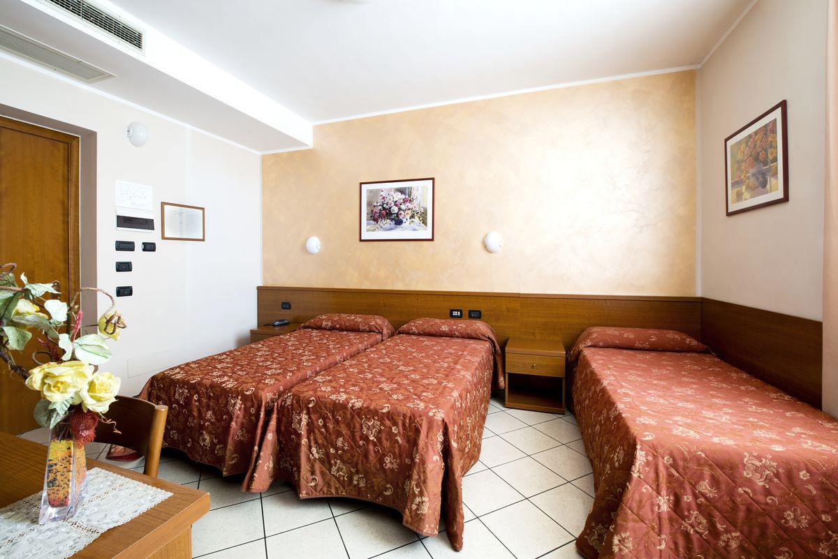 A hotel room with two single beds, a wooden headboard, a small desk with a vase of flowers, and a wall-mounted picture.