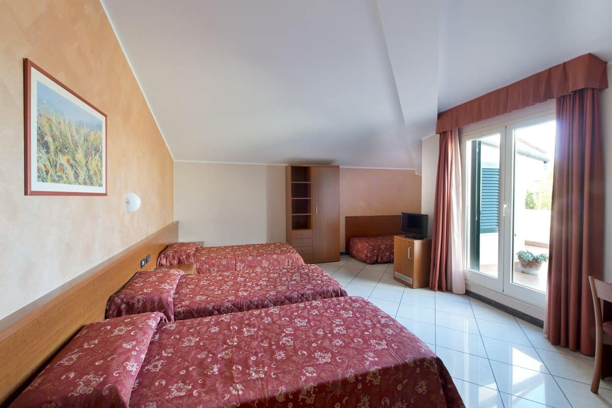 Habitación de hotel con dos camas, televisión, armario y balcón con cortinas.