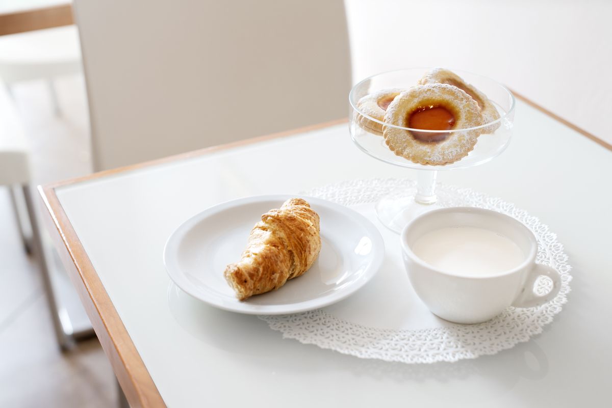 Uma mesa com um croissant, uma sobremesa com recheio de fruta e uma xícara de café.