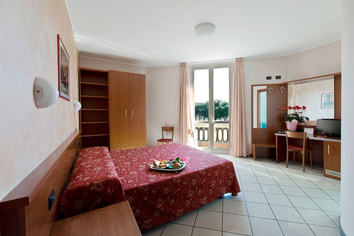Una habitación con cama, escritorio, televisor y balcón con vistas.
