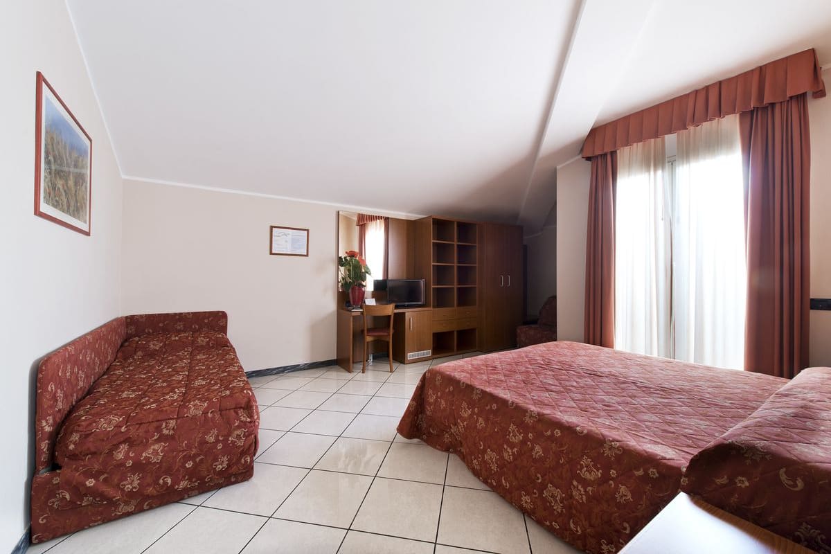 Habitación de hotel con dos camas, un escritorio con computadora, televisión y ventana con cortinas.