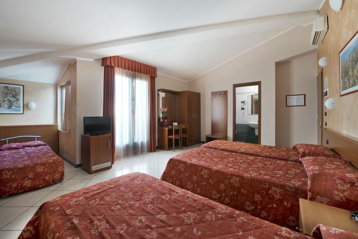 Habitación de hotel con dos camas, televisión, escritorio y baño visible a través de una puerta abierta.