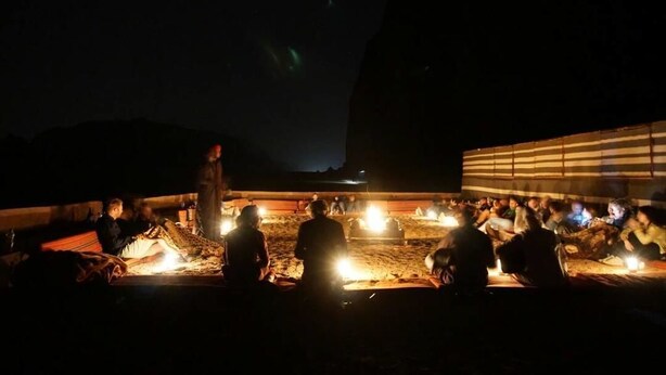 A group of people gathered around a campfire in a desert setting at night. - Wadi Rum Candles Camp (Wadi Rum)
