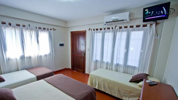A hotel room with two single beds, a TV, an air conditioning unit, and a wooden door.