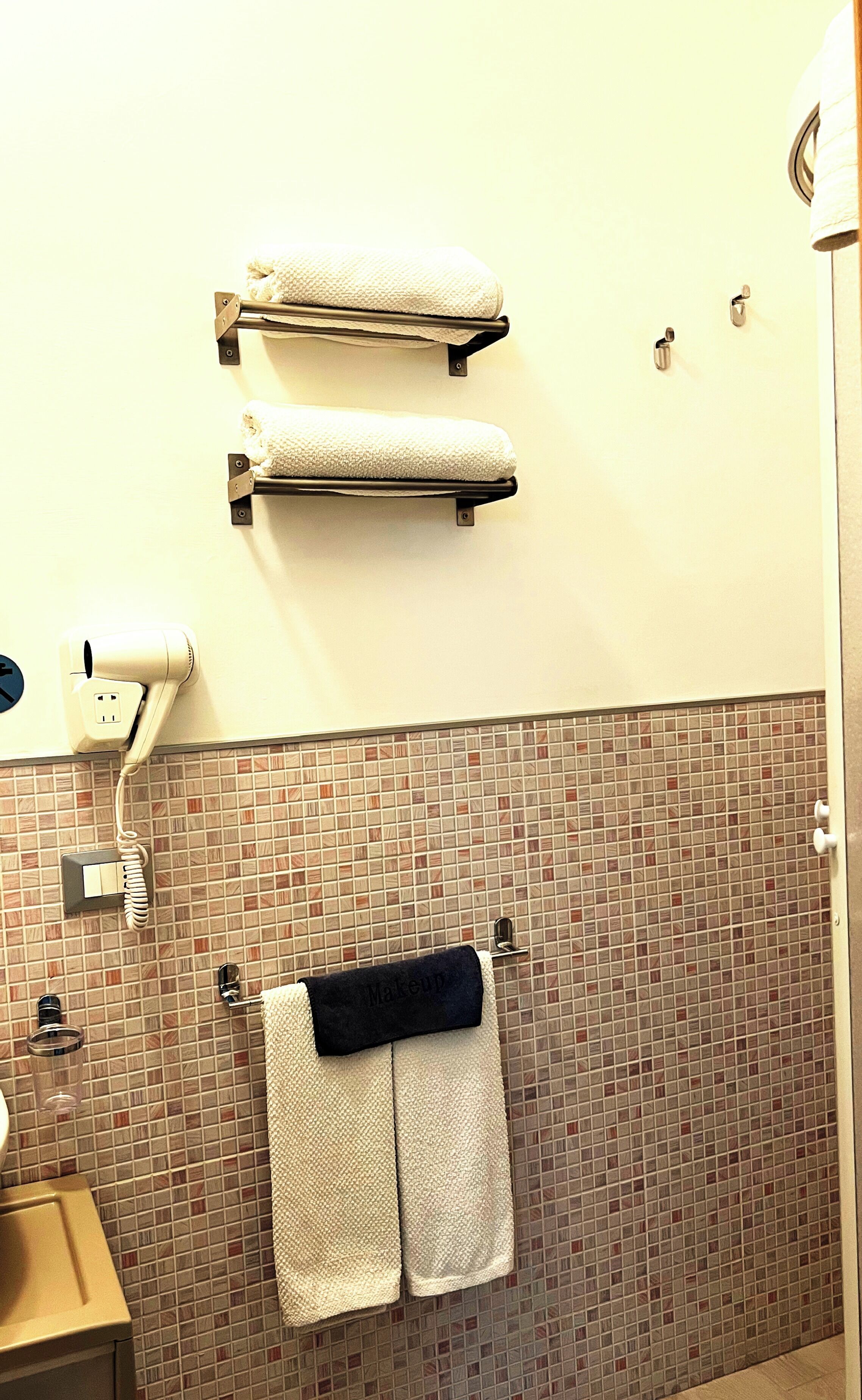 A bathroom with two towel racks holding white towels, a hairdryer, a towel warmer, a tiled backsplash, and a sink with a mirror.