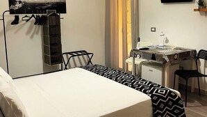 Quarto com cama, escrivaninha, cadeira, televisão e relógio na parede.