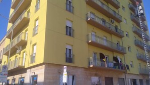 A multi-story yellow building with balconies, a storefront on the ground floor, and parked cars in front. - B&B MaryJosè (Trapani)