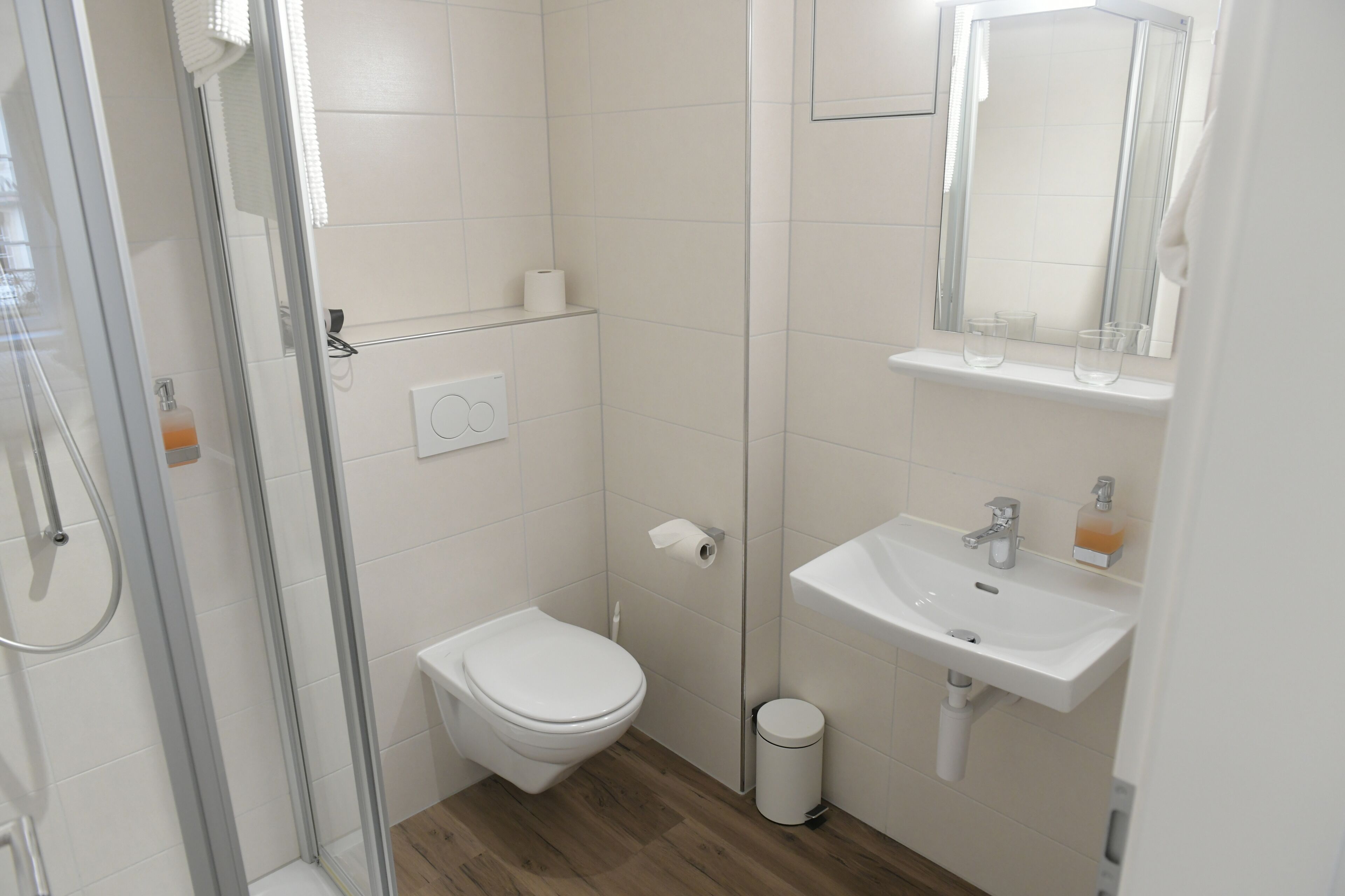 Een moderne badkamer met een douche met glazen wand, een wit toilet en een wastafel met spiegel.