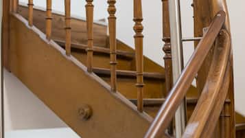 Una escalera de madera con barandilla de metal y una pared blanca con un letrero de salida de emergencia verde.