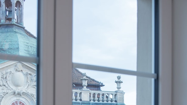 A view through a window of a building with classical architecture, including a clock and decorative elements. - Albergo Diffuso (Porrentruy)