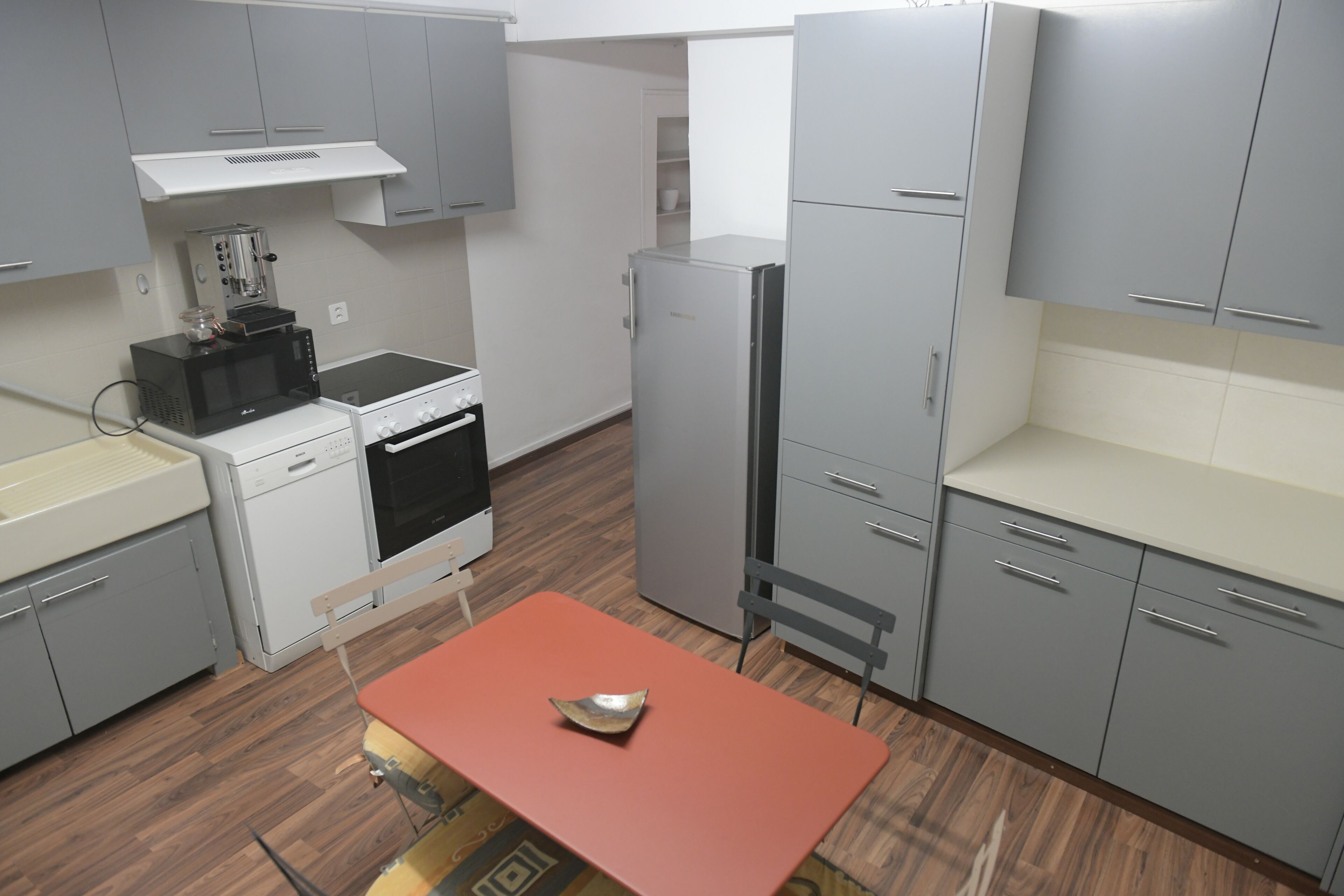Une cuisine de taille réduite avec des meubles gris, un four à micro-ondes, un lave-vaisselle et un réfrigérateur.