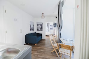 A modern, well-lit room with a sofa, a dining table, and a view of the street through large windows. - Albergo Diffuso (Porrentruy)