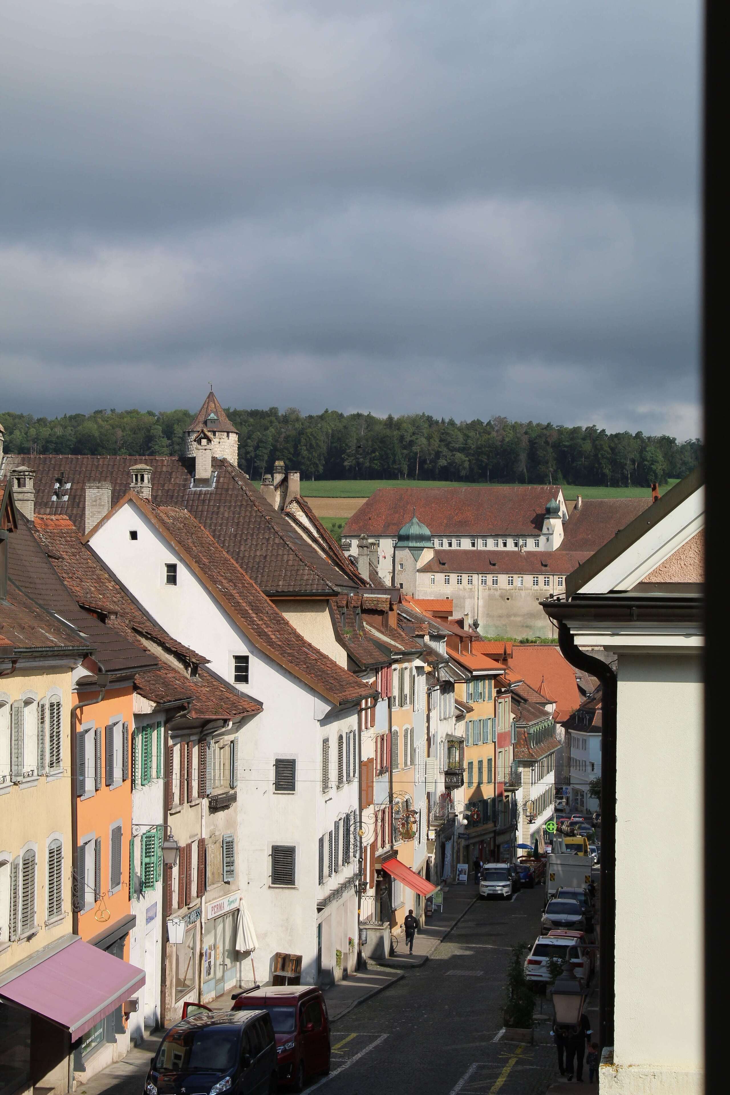 Eine enge Straße, gesäumt von bunten Häusern, mit einer Burg im Hintergrund und wolkenlosem Himmel.