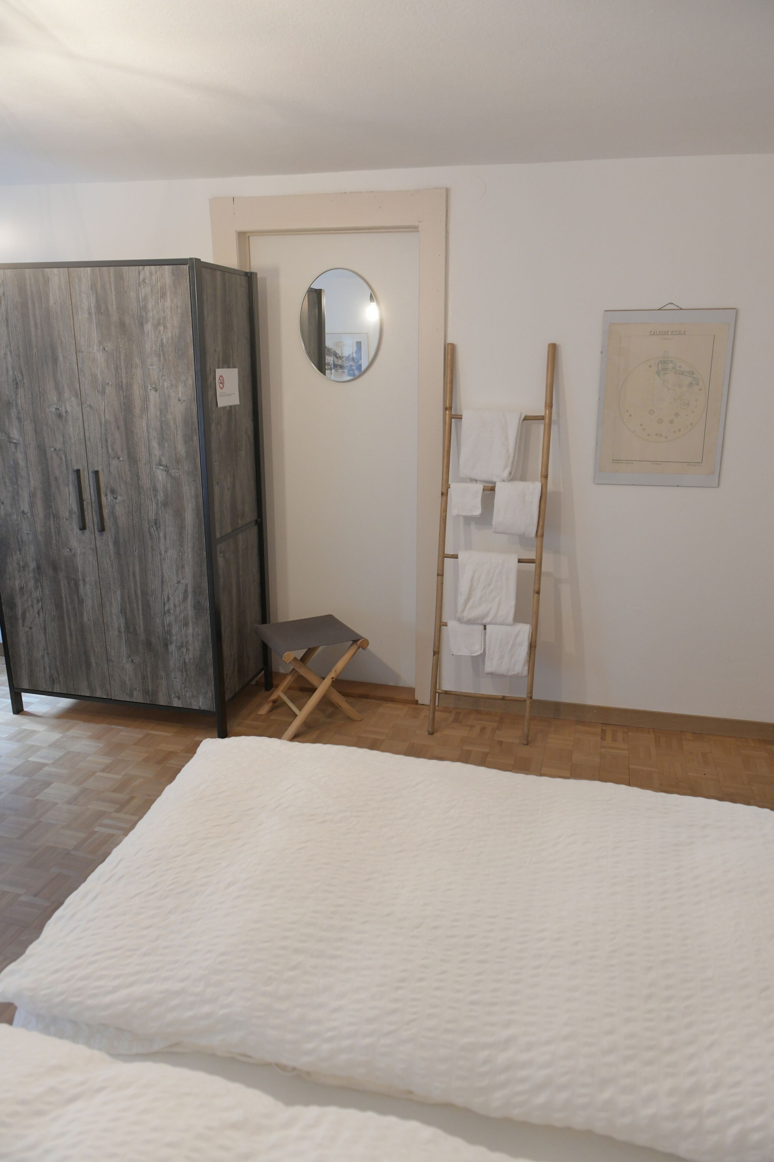 Una habitación con un armario grande, una mesita, una escalera con toallas, un espejo y un cuadro en la pared.