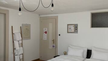 A bedroom with a wooden bed, white bedding, a ladder with towels, a door with a sign, and a light fixture.