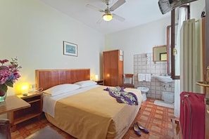 A hotel room with a bed, bedside table, lamp, and a view of the bathroom. - Albergo Al Gobbo   (Venice)
