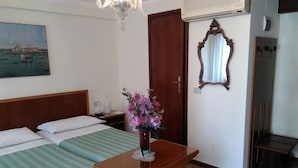 A hotel room with two beds, a wooden table with a vase of flowers, a painting on the wall, a mirror, and a door. - Albergo Al Gobbo   (Venice)