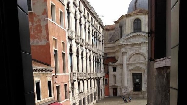 A courtyard with a red awning, a fountain, and a building with classical architecture. - Albergo Al Gobbo   (Venice)