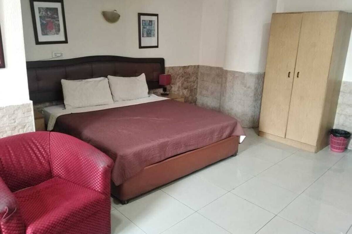 Une chambre à coucher avec un lit, une chaise rouge, une armoire et deux tableaux encadrés accrochés au mur.