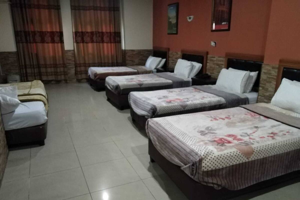 Une chambre d’hôtel avec quatre lits alignés, chacun recouvert d’une courtepointe à motifs floraux et agrémenté d’oreillers blancs.