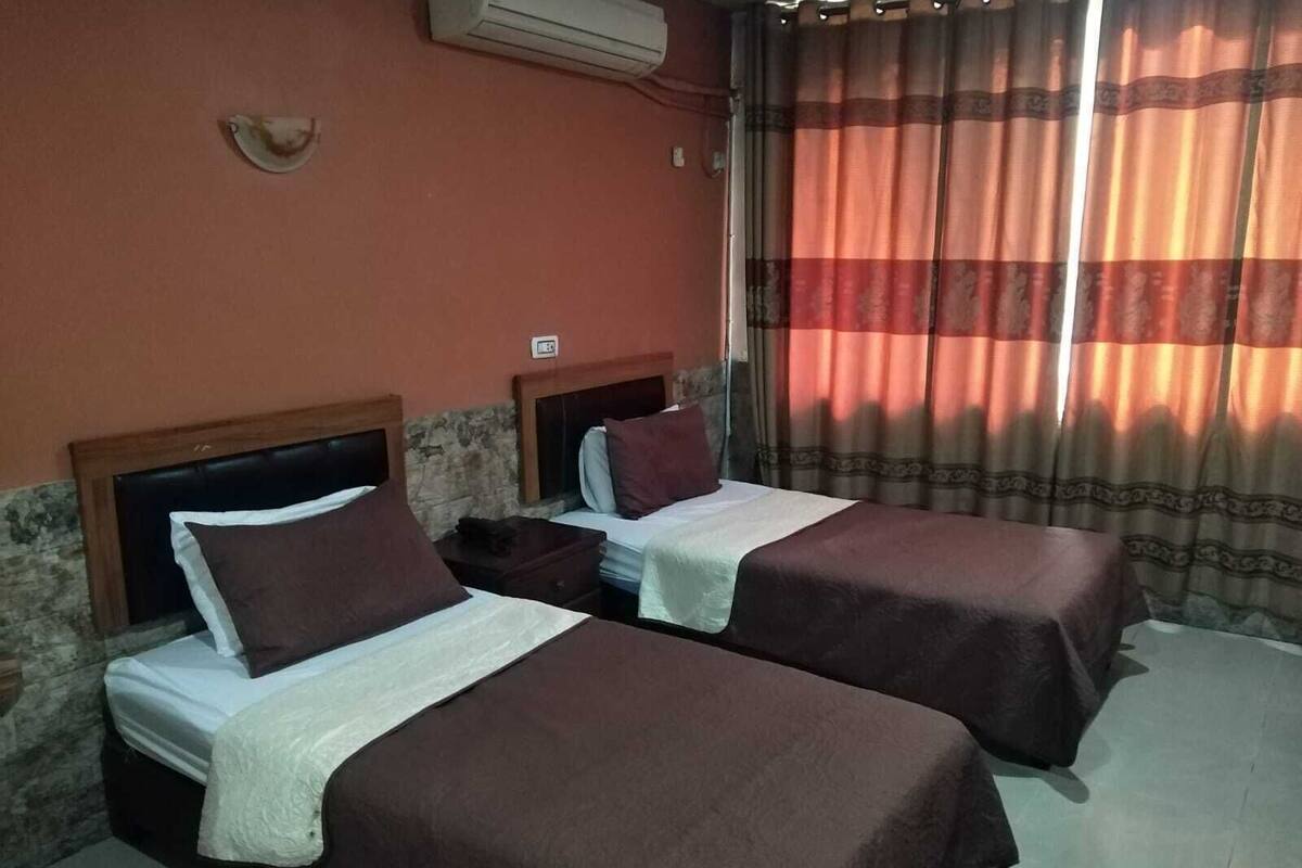 Une chambre d’hôtel avec deux lits, chacun doté d’une tête de lit, d’une table de chevet et d’une lampe.