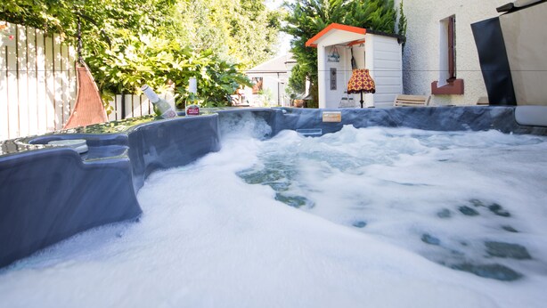 A hot tub with a waterfall feature, surrounded by a fence and greenery. - JustB (Edinburgh)