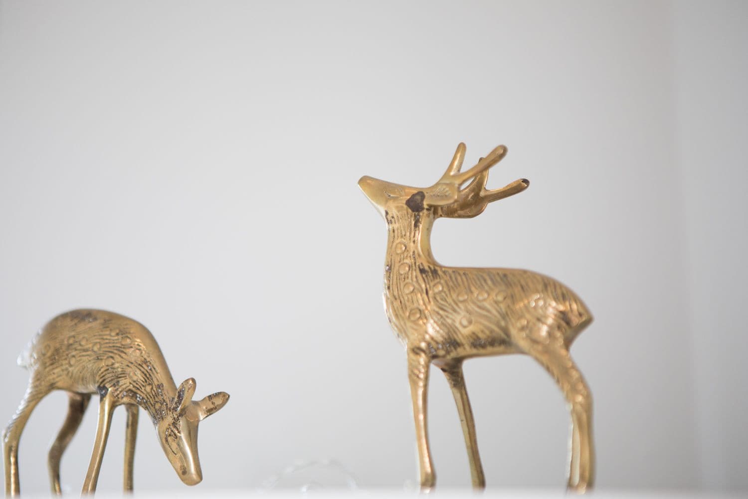 Two golden deer figurines on a white surface against a plain background.