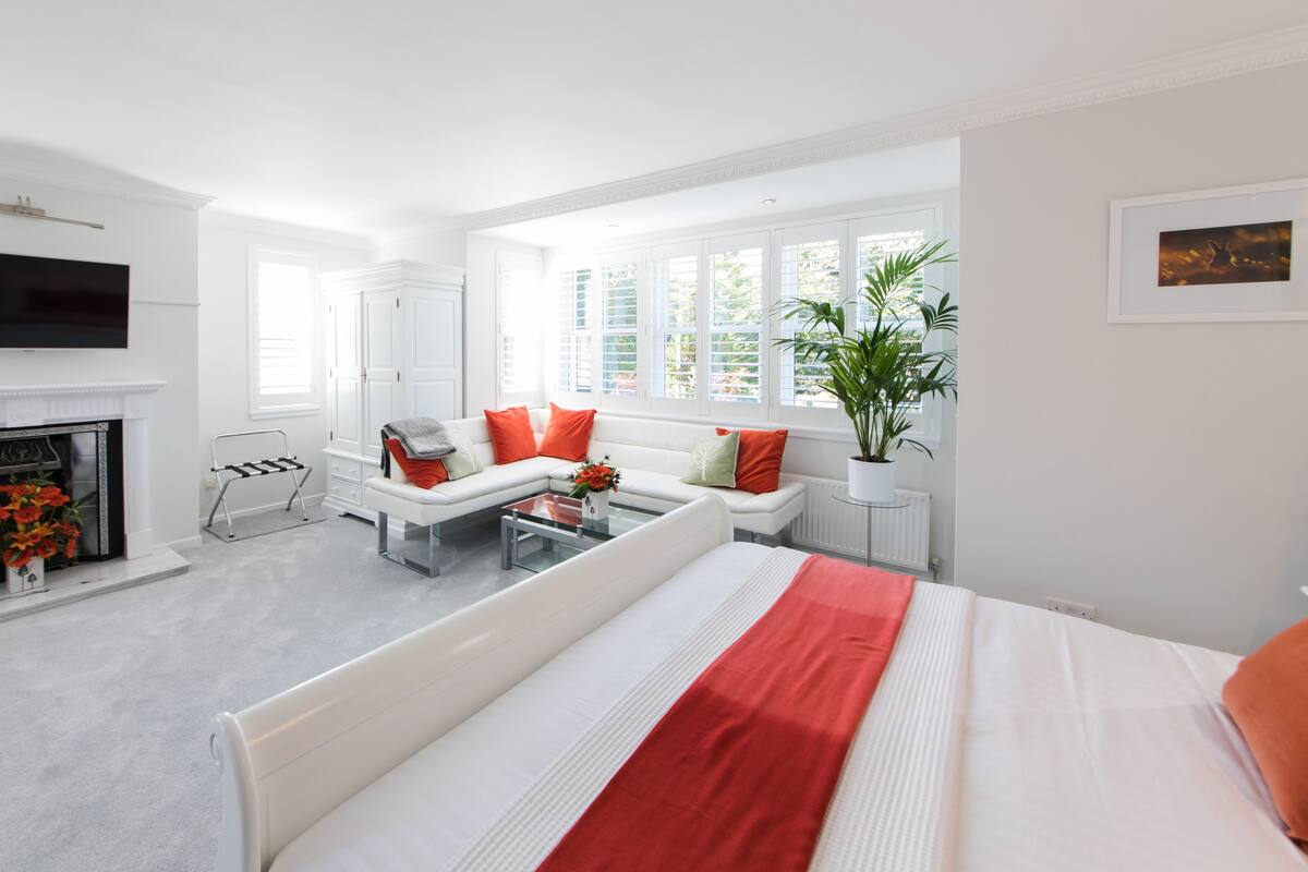 A modern bedroom with a large bed, a sofa, a coffee table, and a fireplace.